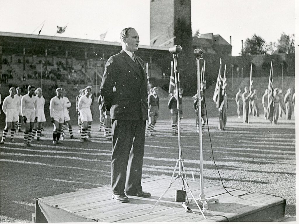 Bilde av Olaf Helset som taler han under åpningen av et stevne på Stockholms Olympiastadion i august 1944
